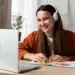 Pessoa sorrindo enquanto estuda em casa com fones de ouvido e usando post-its coloridos para organizar suas anotações.