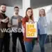 Imagem com grupo de profissionais segurando cartaz com o título 'Vagas de Emprego' e mostrando positividade, representando uma oportunidade de trabalho para Atendente HOME OFFICE.