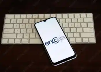 Imagem de um smartphone com o logo do Encceja 2025 exibido na tela, sobre uma mesa com um teclado branco ao fundo.