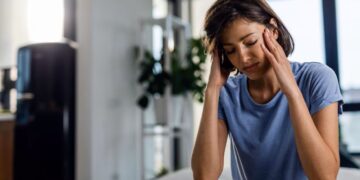 Mulher com dor de cabeça, com as mãos na cabeça e expressão de desconforto, indicando sinais de esgotamento emocional.