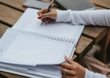 Pessoa escrevendo em um calendário em um dia tranquilo, com um caderno e caneta.