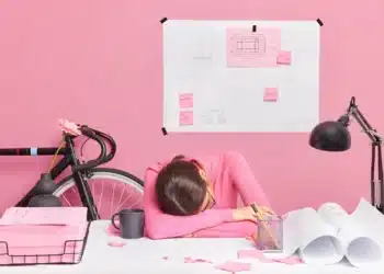 Pessoa sentada em frente a uma mesa com papéis e post-its, simbolizando a procrastinação e sobrecarga de tarefas