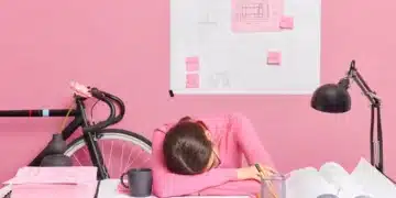 Pessoa sentada em frente a uma mesa com papéis e post-its, simbolizando a procrastinação e sobrecarga de tarefas