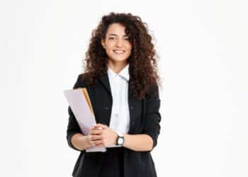 Mulher jovem com cabelo cacheado segurando documentos, pronta para começar estágio profissional.