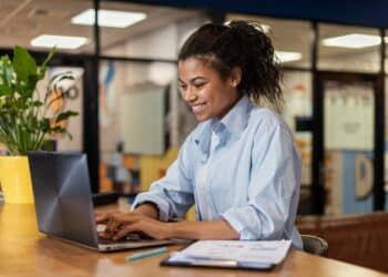 Mulher concentrada digitando no laptop em ambiente de escritório moderno e colorido.
