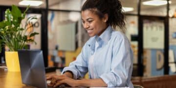 Mulher concentrada digitando no laptop em ambiente de escritório moderno e colorido.