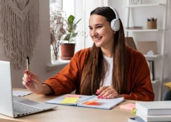 Jovem estudando em casa com fones de ouvido e material de estudo.