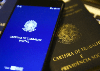 Celular mostrando aplicativo da Carteira de Trabalho Digital sobre carteira física da CLT