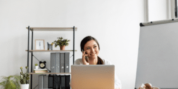 Mulher sorridente trabalhando remotamente em um notebook e falando ao telefone em ambiente organizado