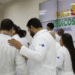 Grupo de médicos em jalecos do SUS conversando em frente a um painel com mapa do Brasil e texto “Mais Médicos para o Brasil”