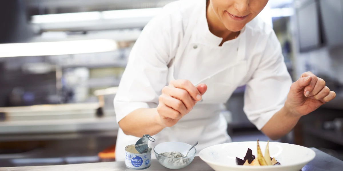 Chef em cozinha profissional, decorando prato com técnica refinada.
