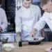 Três chefs trabalhando juntos em cozinha, com foco em pratos sofisticados.