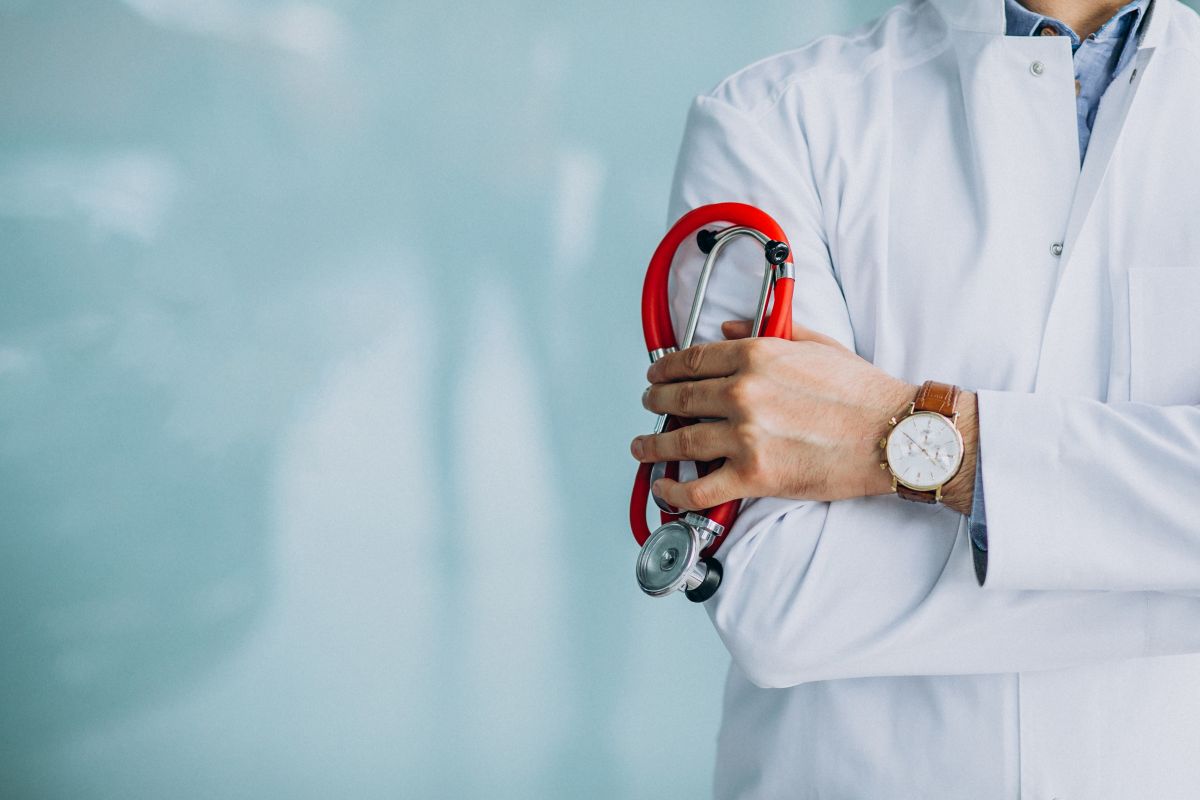 Médico segurando estetoscópio com jaleco branco, representando atuação na atenção básica de saúde.