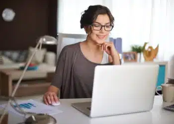 Mulher trabalhando no computador em casa, com sorriso no rosto