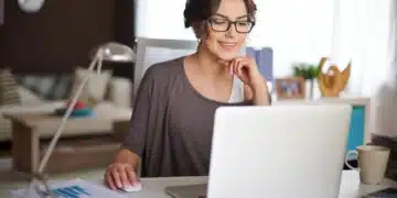 Mulher trabalhando no computador em casa, com sorriso no rosto
