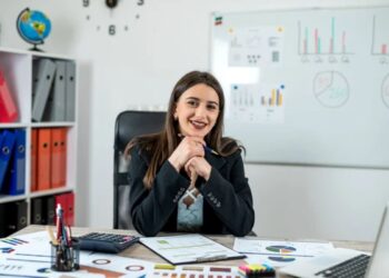 Mulher sorridente sentada em mesa com documentos e gráficos em escritório corporativo