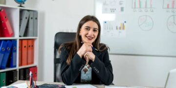 Mulher sorridente sentada em mesa com documentos e gráficos em escritório corporativo