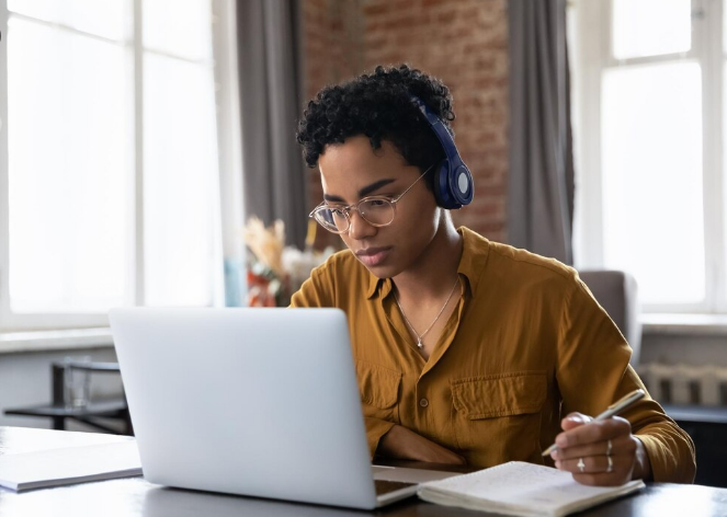 Jovem estudando online com fones de ouvido e fazendo anotações durante curso técnico a distância