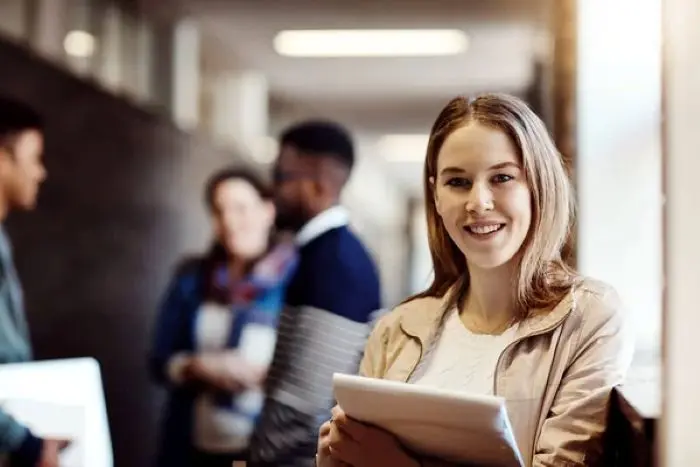Jovem sorrindo enquanto segura um tablet em um ambiente educacional moderno