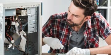 Técnico masculino trabalhando na manutenção interna de um computador aberto usando luvas brancas