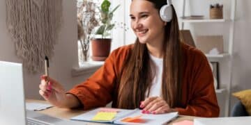 Mulher sorrindo enquanto estuda em frente ao laptop, com post-its coloridos sobre a mesa, simbolizando organização e técnica Pomodoro.