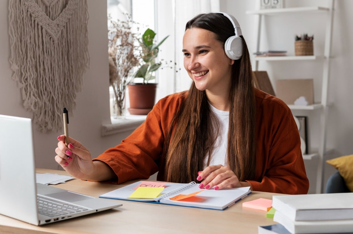 Estudante usando fones de ouvido e estudando em casa com laptop e caderno.