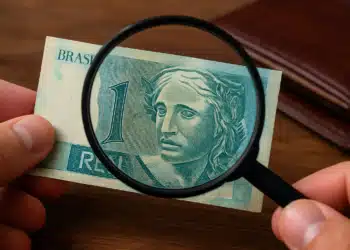 Pessoa examinando uma cédula rara de 1 real com uma lupa