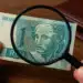 Pessoa examinando uma cédula rara de 1 real com uma lupa