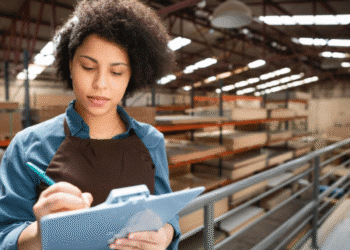 Técnica em logística anotando informações em galpão industrial