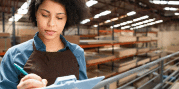 Técnica em logística anotando informações em galpão industrial