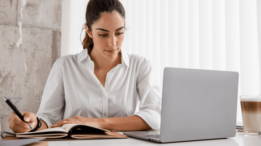 Mulher estudando on-line para concurso público com caderno e notebook