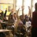 Estudantes levantando as mãos em sala de aula durante uma explicação.