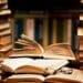 Foto detalhada de livros empilhados, com páginas abertas e óculos sobre um livro, simbolizando o estudo e a leitura.
