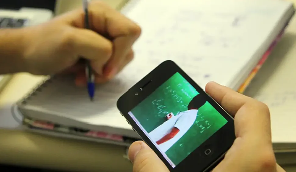 Estudante assistindo a uma aula online e anotando em caderno, representando a adaptação ao ensino a distância (EAD).