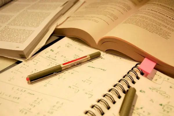 Materiais de estudo com livros, anotações de matemática e canetas coloridas, ilustrando um ambiente de estudo organizado.
