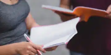 Estudantes interagindo enquanto estudam, com cadernos e canetas em mãos."