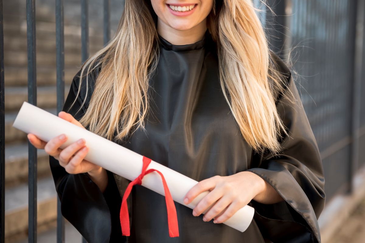 Formanda com beca segurando diploma e capelo em celebração à conclusão do curso*