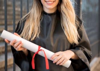 Mulher sorrindo com beca de formatura segurando diploma enrolado com fita vermelha