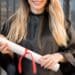 Mulher sorrindo com beca de formatura segurando diploma enrolado com fita vermelha