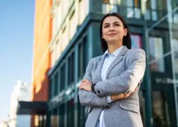 Mulher de negócios posando ao ar livre com os braços cruzados, com um sorriso confiante e expressão de liderança.