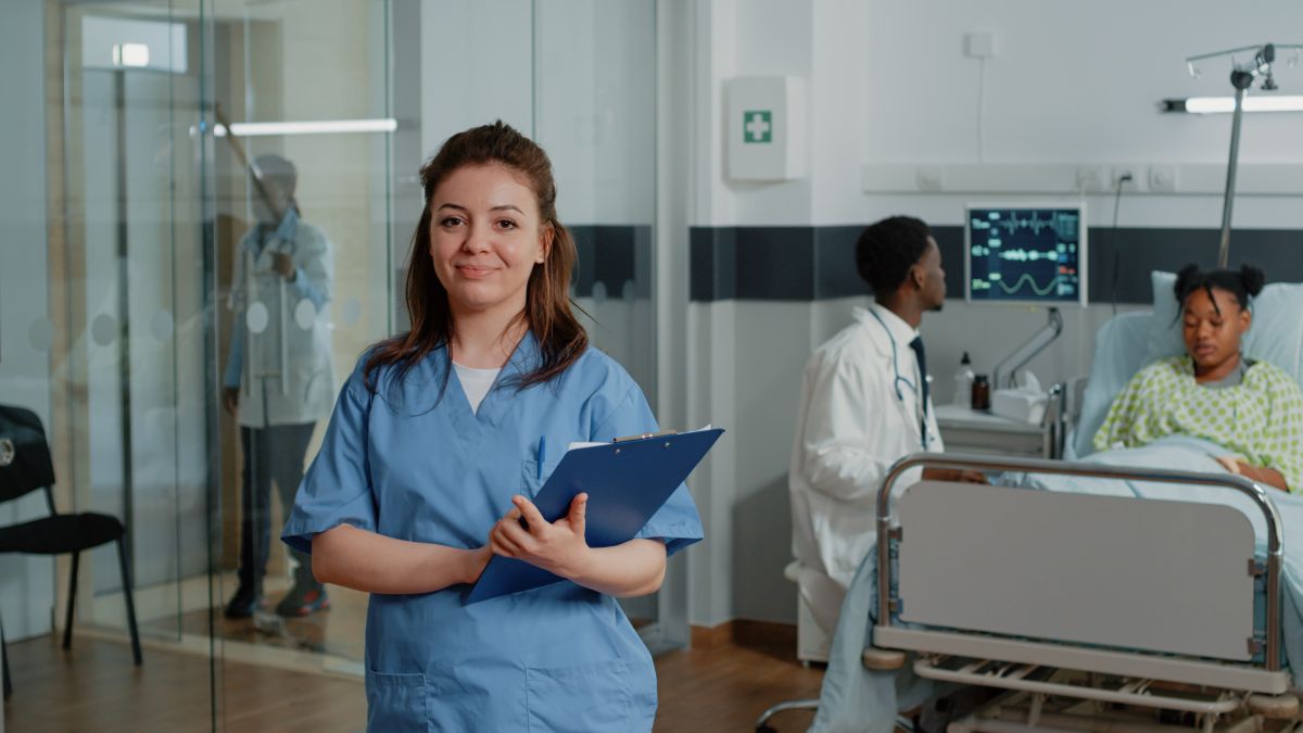 Técnica em enfermagem com prancheta sorrindo em ambiente hospitalar