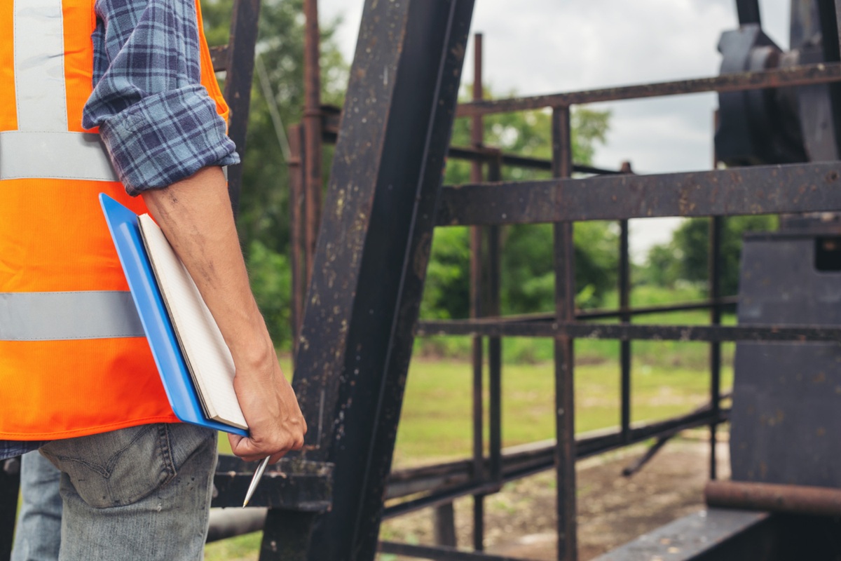 Profissional de Defesa Civil usando colete de segurança e segurando um caderno de anotações no local de trabalho.