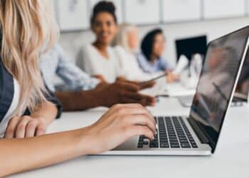 Pessoa digitando no laptop durante uma reunião, simbolizando as inscrições abertas para programas de trainee com alta remuneração.