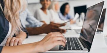 Pessoa digitando no laptop durante uma reunião, simbolizando as inscrições abertas para programas de trainee com alta remuneração.