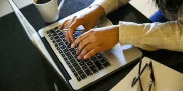 Pessoa digitando no notebook com uma xícara de café ao lado, simbolizando a capacitação e qualificação profissional de jovens na plataforma de cursos gratuitos do governo.