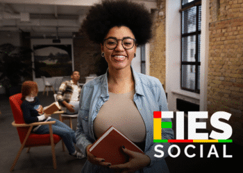 Estudante sorrindo em ambiente de estudo, com outros colegas ao fundo, representando a oportunidade de convocação para o FIES 2025.2.