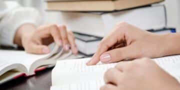 Duas mãos folheando livros abertos, simbolizando o processo de revisão de texto e estudo.