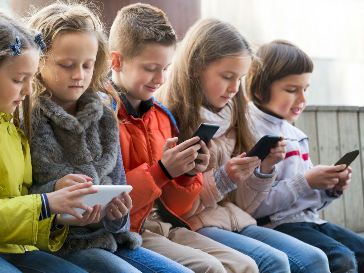 Grupo de crianças sentadas, concentradas em seus smartphones e tablets, ilustrando o uso crescente da tecnologia na infância e o debate sobre o "PL da Adultização".