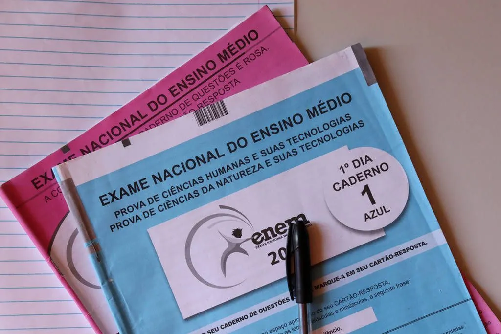 Provas do Exame Nacional do Ensino Médio (Enem) com cadernos e caneta sobre uma mesa.