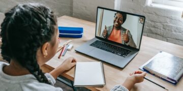 Estudante interagindo com tutor em videochamada durante aula online, em sua rotina de estudos.